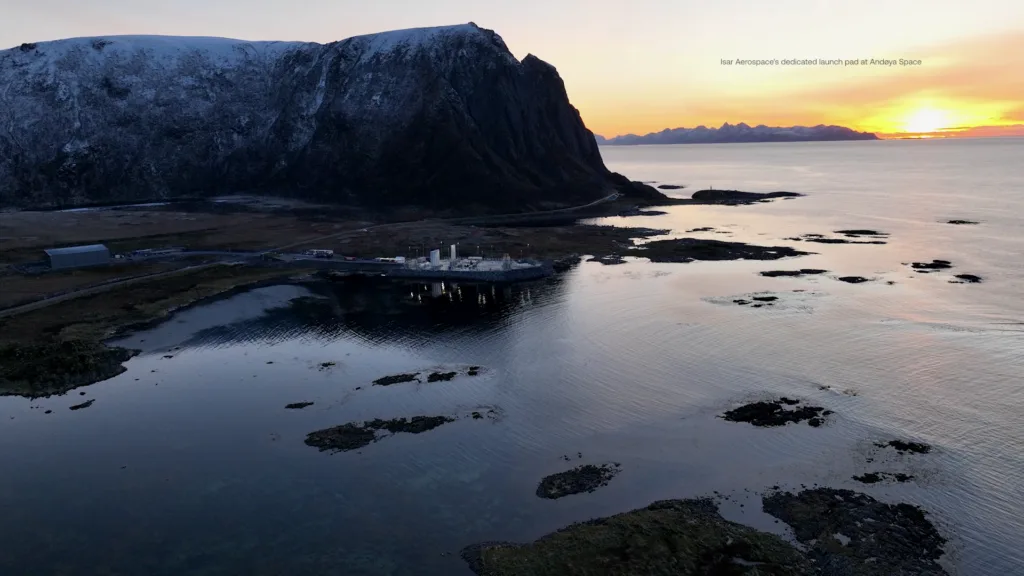 Aerial view of the Andøya Spaceport launch pad on the Norwegian coast below a snow-capped cliff at sunset