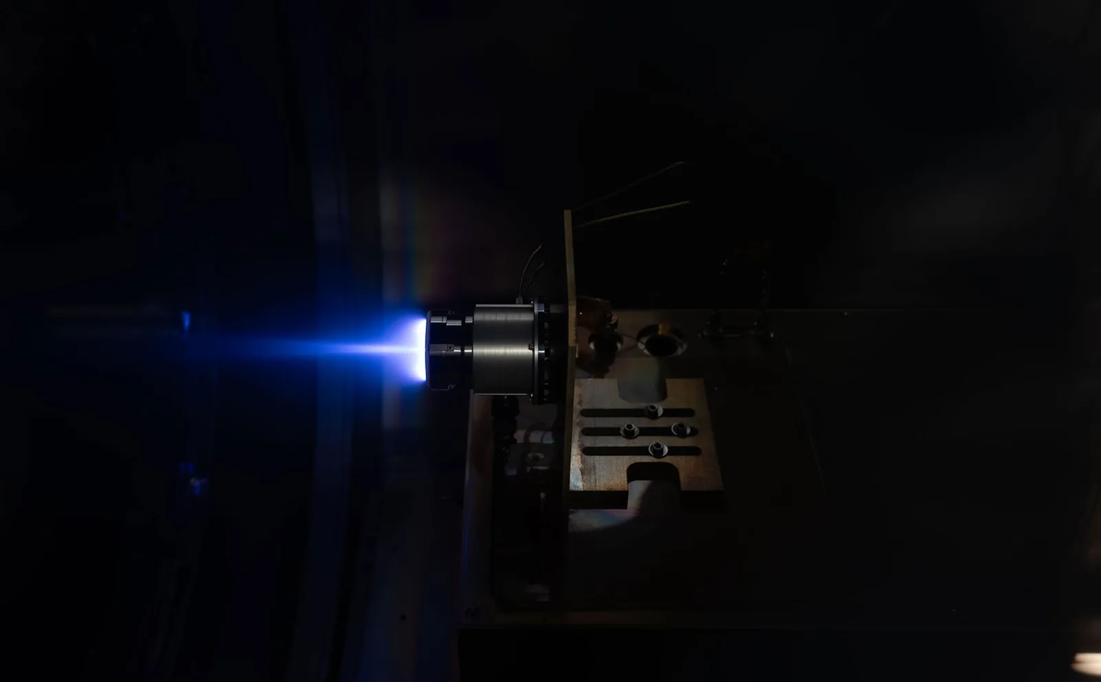 An Astra Spacecraft Engine thruster firing with a blue plasma plume inside a vacuum test chamber