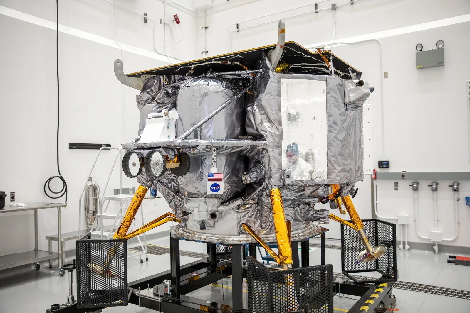Astrobotic's Peregrine lunar lander, wrapped in silver insulation on gold landing legs, in a clean room at the Astrotech facility in Florida