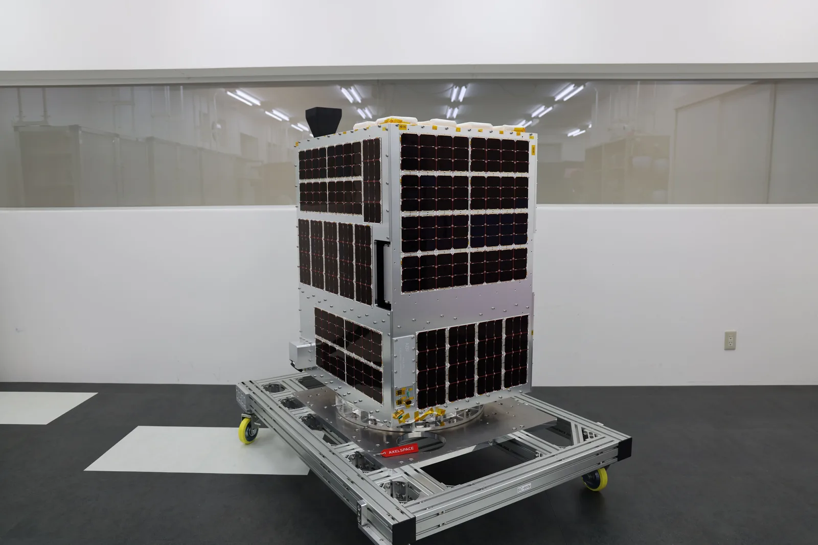 An Axelspace AxelLiner satellite covered in solar cells standing on a handling frame in a clean room