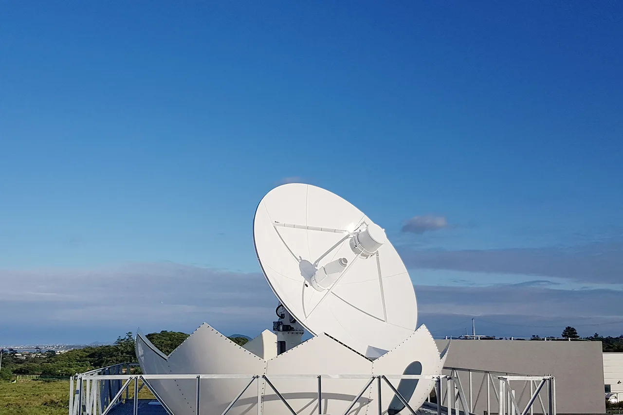 A CONTEC ground station dish antenna pointed skyward on its rooftop platform under a blue sky