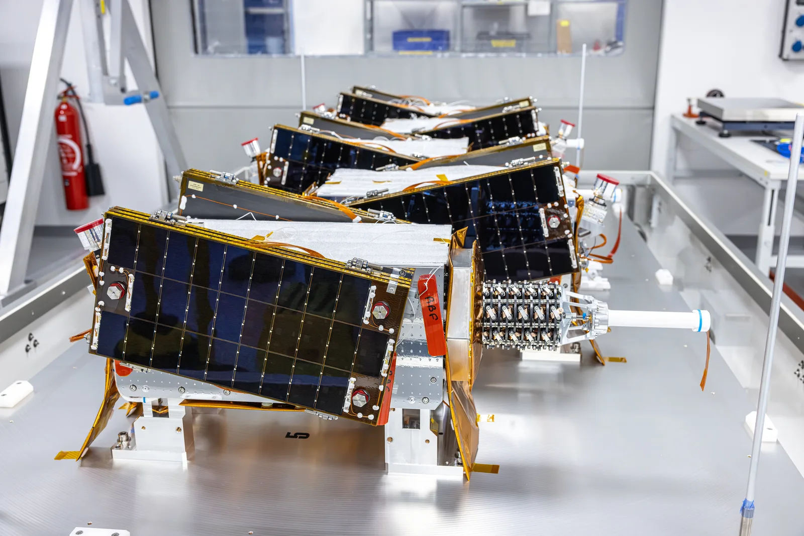 Several Kinéis nanosatellites with deployed solar panels lined up in a clean room