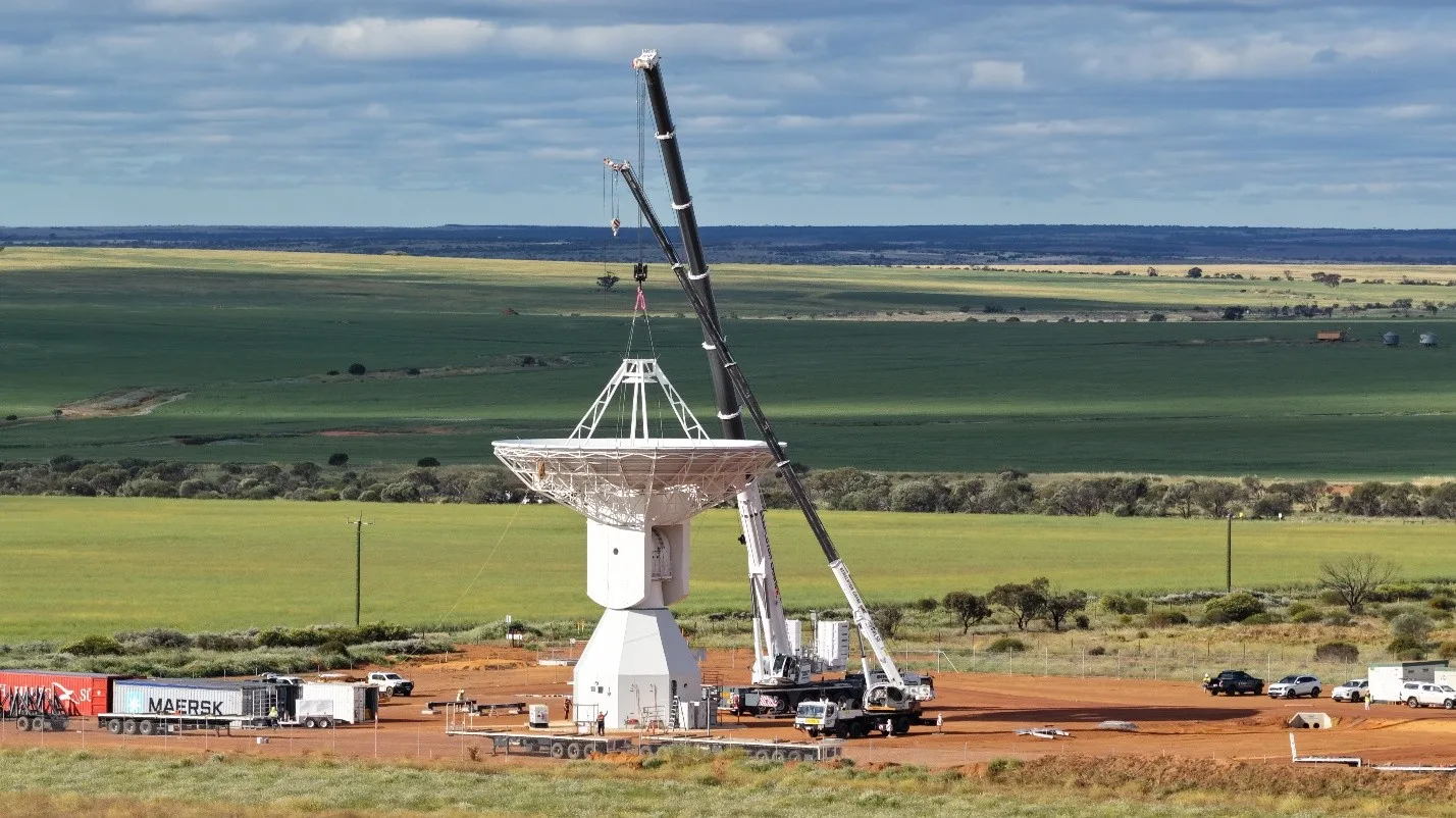 Crane lifting a large KSAT dish antenna for lunar communications into place on farmland