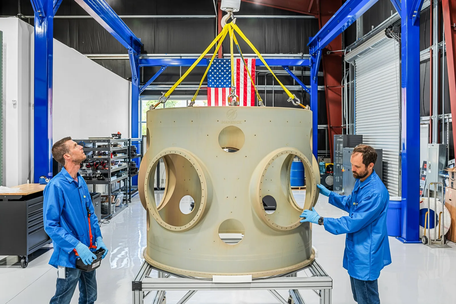 Two Maverick engineers inspecting a large payload adapter ring hanging from a crane in their integration facility