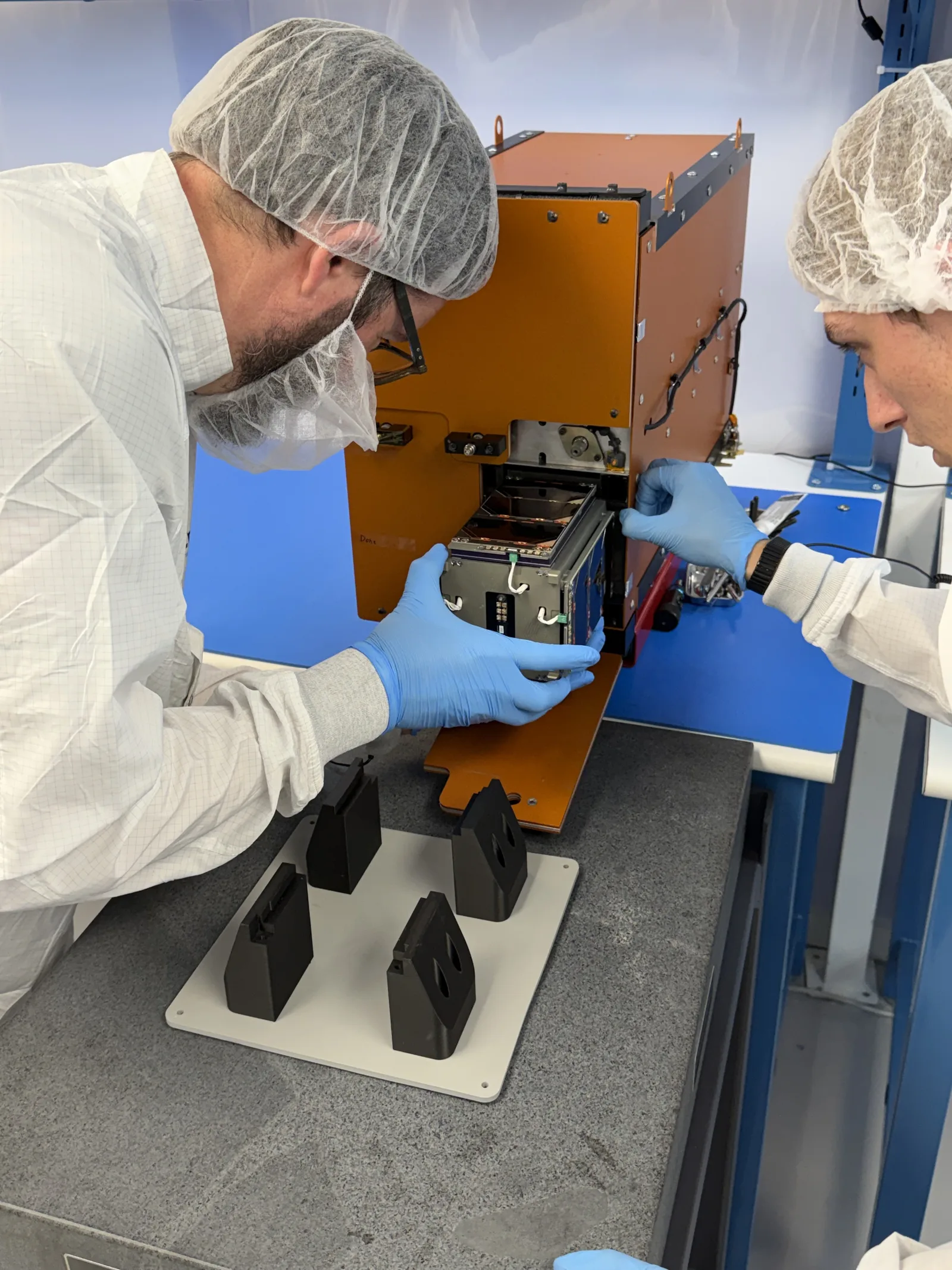 Technicians in a cleanroom loading a customer cubesat into a SEOPS deployer for a rideshare mission
