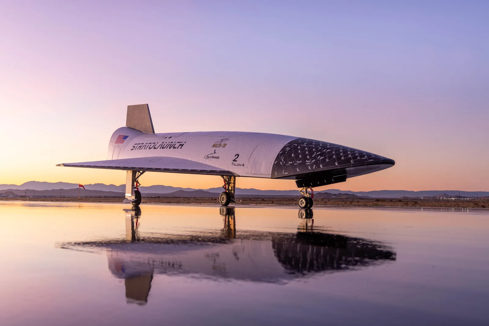 The Talon-A2 hypersonic vehicle on its landing gear at sunset, reflected in standing water on the runway
