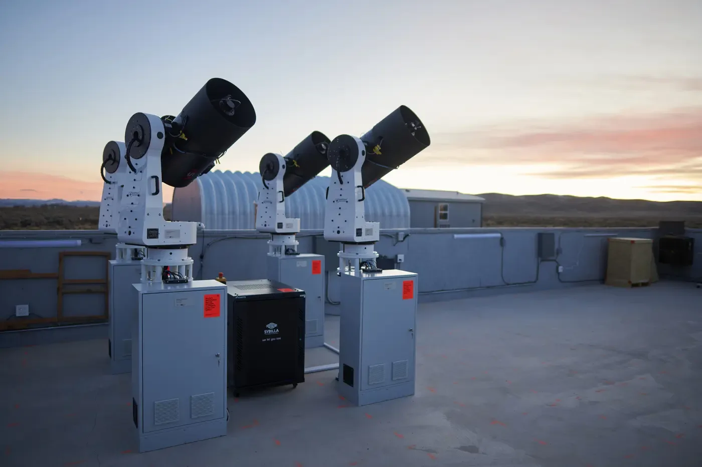Three of Sybilla's robotic tracking telescopes on their mounts at an observing site at dusk