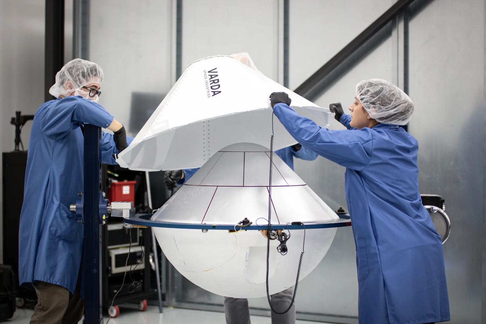 Technicians in cleanroom gowns fit the heat shield onto a Varda W-series reentry capsule during assembly