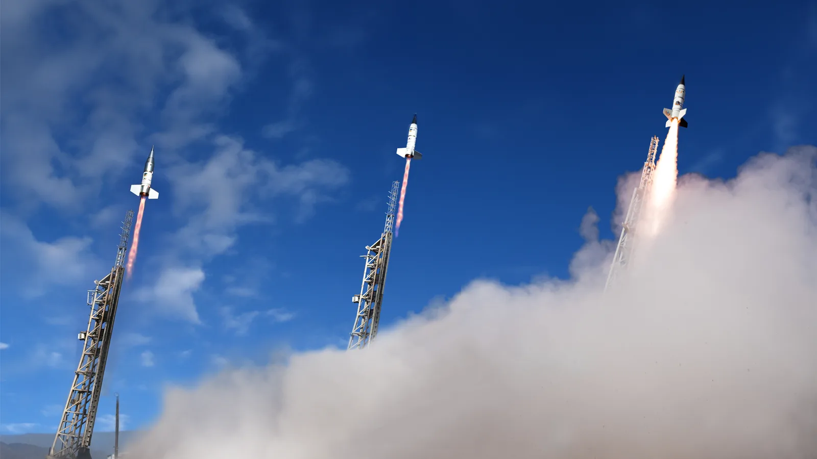 Three X-Bow solid-fueled rockets lifting off from launch rails into a blue sky